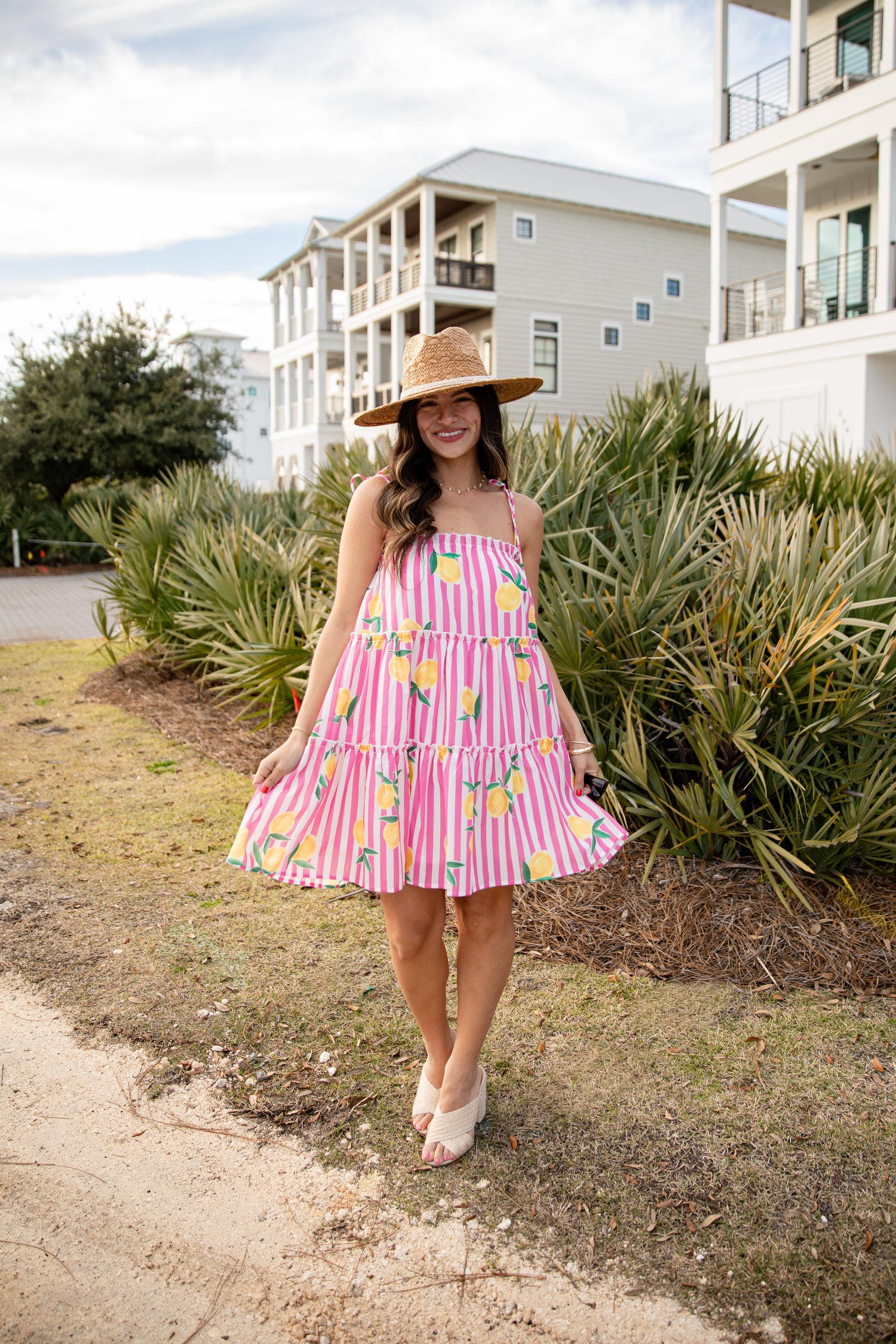 Woman in a pink dress with yellow pineapple pattern and straw hat walking outdoors.