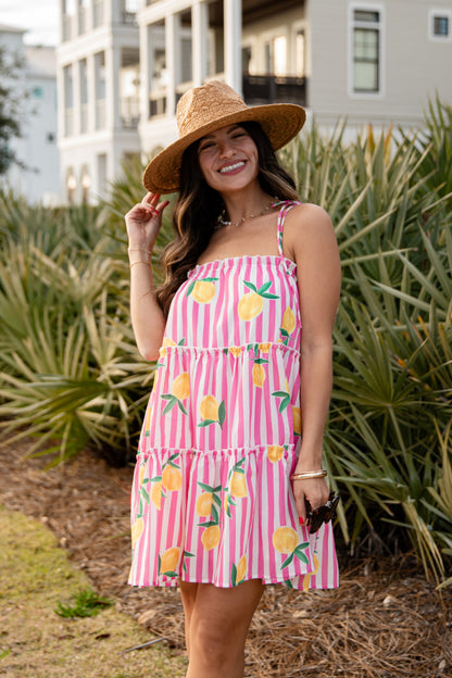Woman wearing a pink dress with lemon print and a straw hat, standing outdoors.