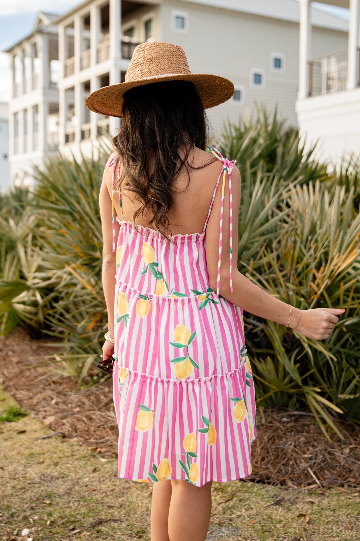 Woman in a pink dress with lemon pattern and straw hat standing outdoors.