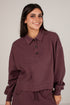 A woman wearing a dark plum-colored long-sleeve polo shirt with a buttoned collar, paired with matching pants, photographed against a neutral light gray background.