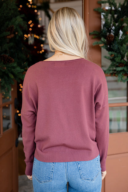 Person wearing a mauve sweater and blue jeans standing in front of Christmas trees.