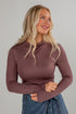 Woman wearing a mauve long-sleeve top against a gray background