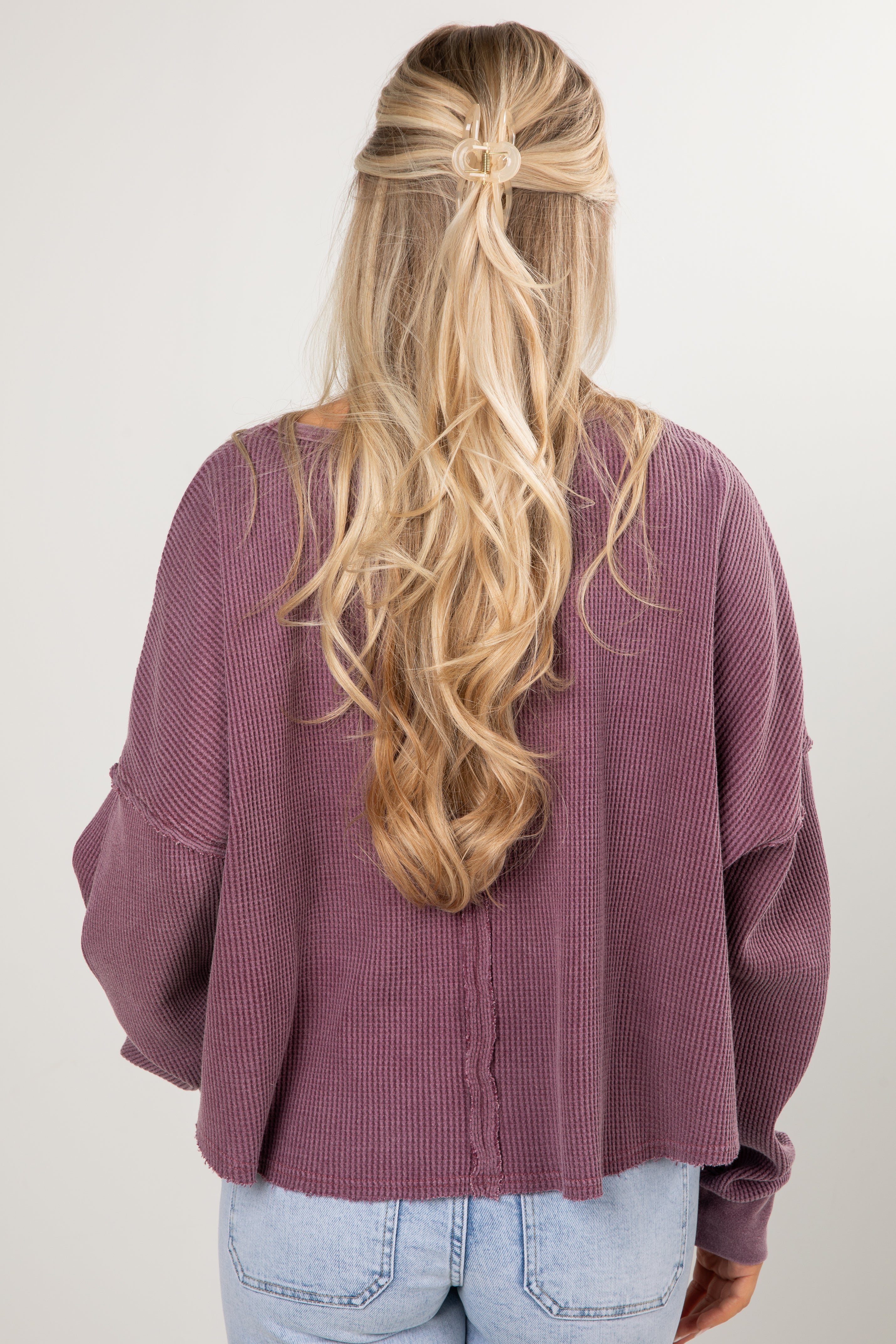 Person wearing a purple cardigan with long blonde hair over one shoulder on a white background