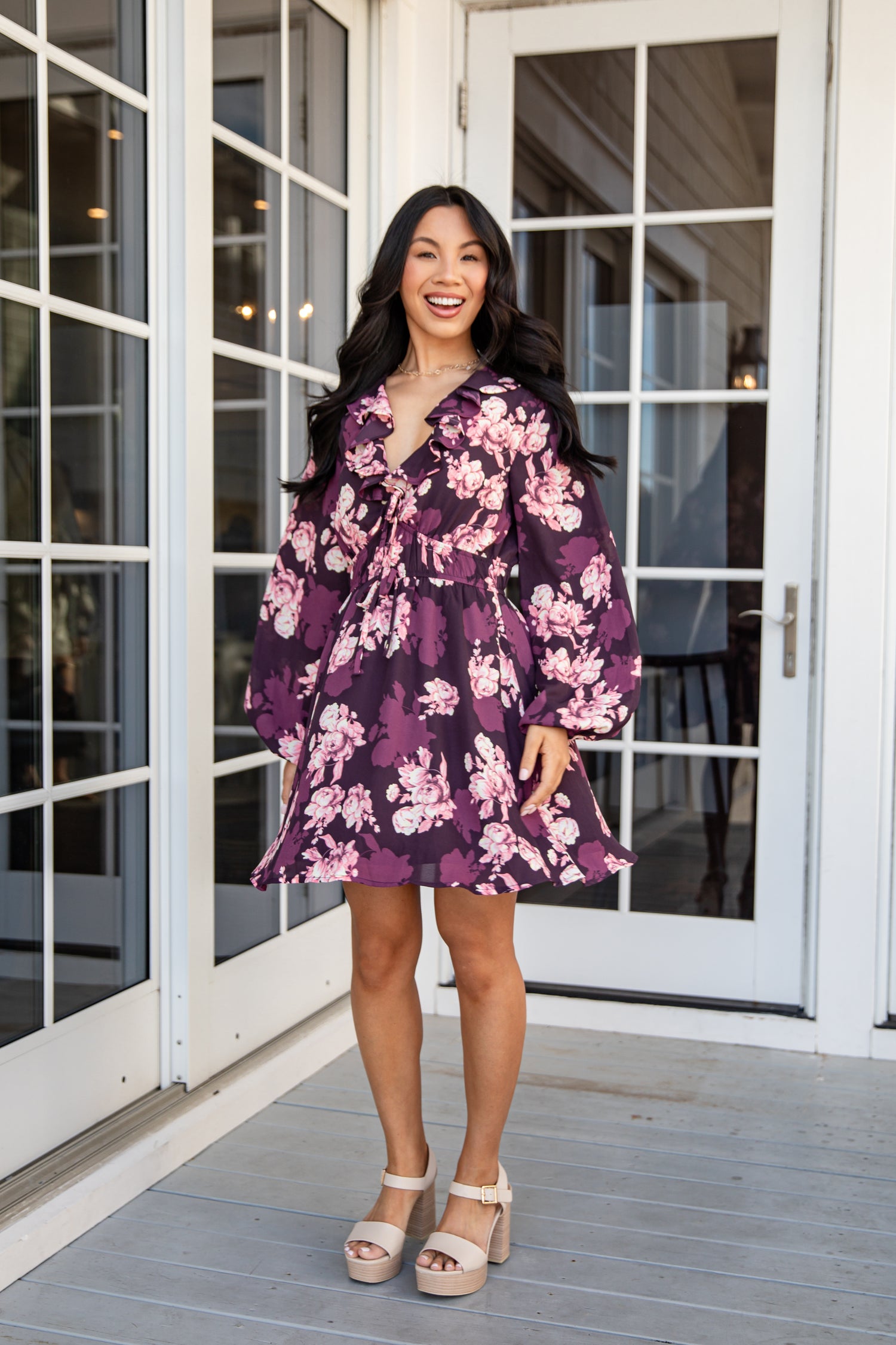 Woman wearing a purple floral dress standing on a wooden deck.