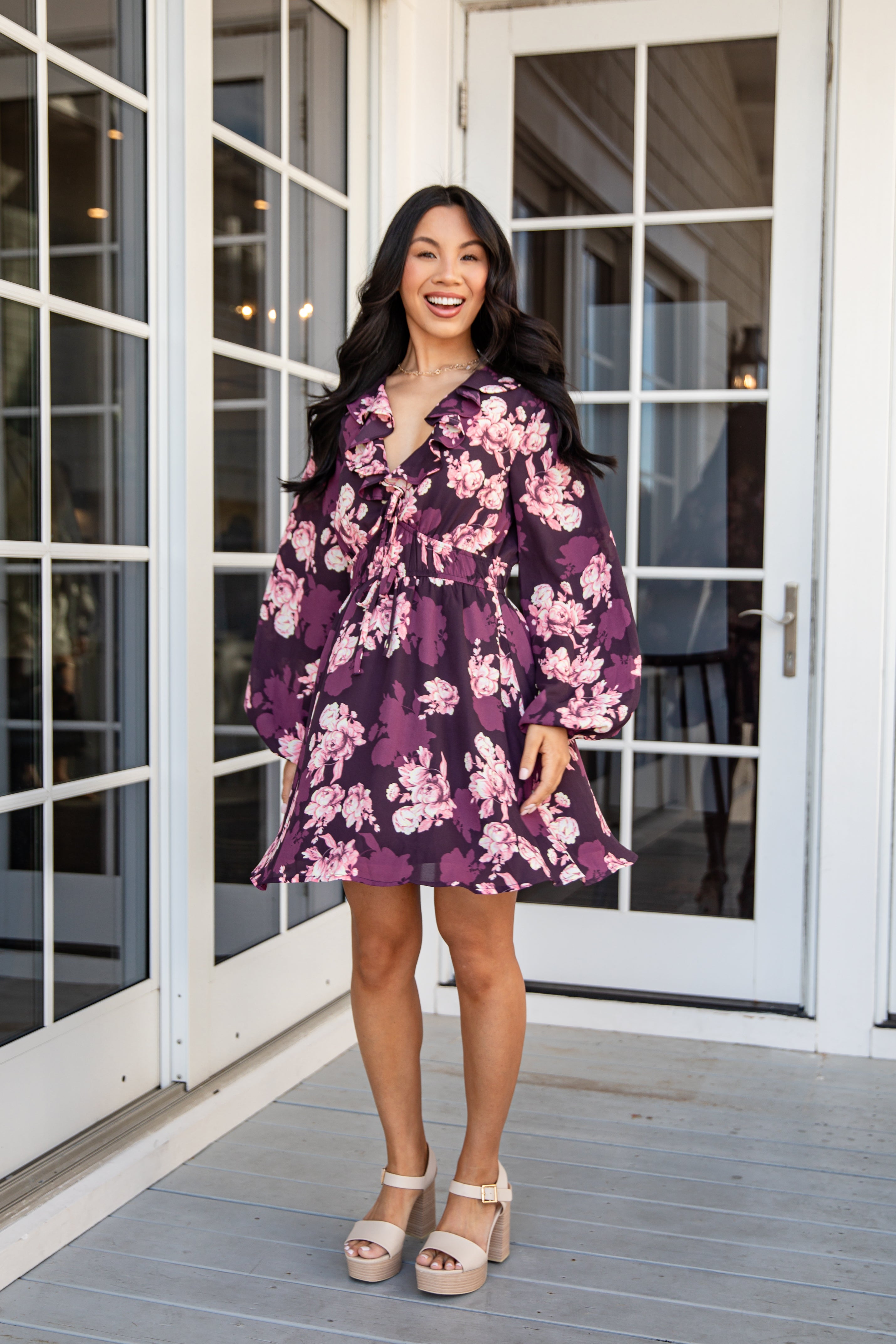 Woman wearing a purple floral dress standing on a wooden deck.