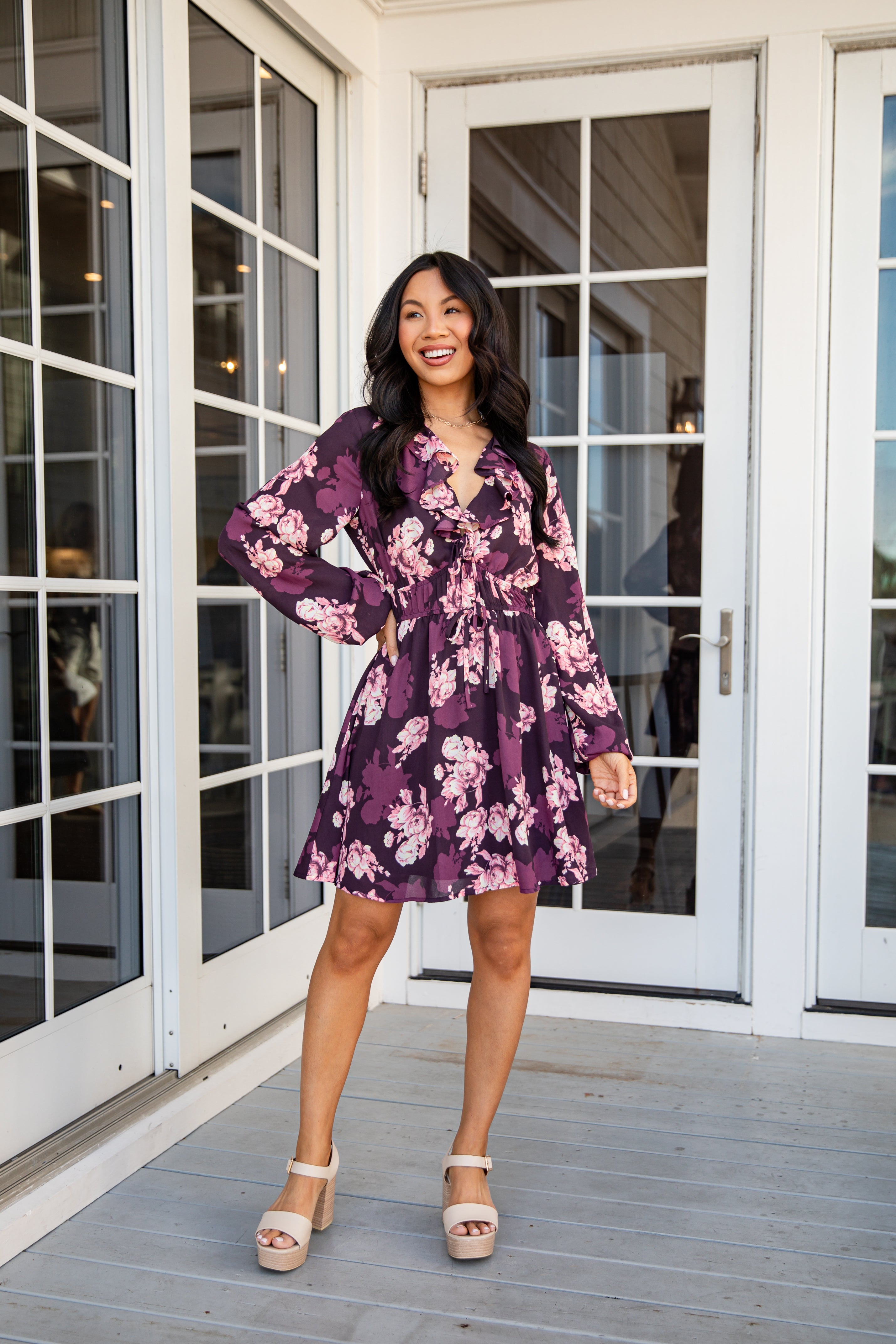 Woman in a purple floral dress standing on a wooden deck with glass doors in the background