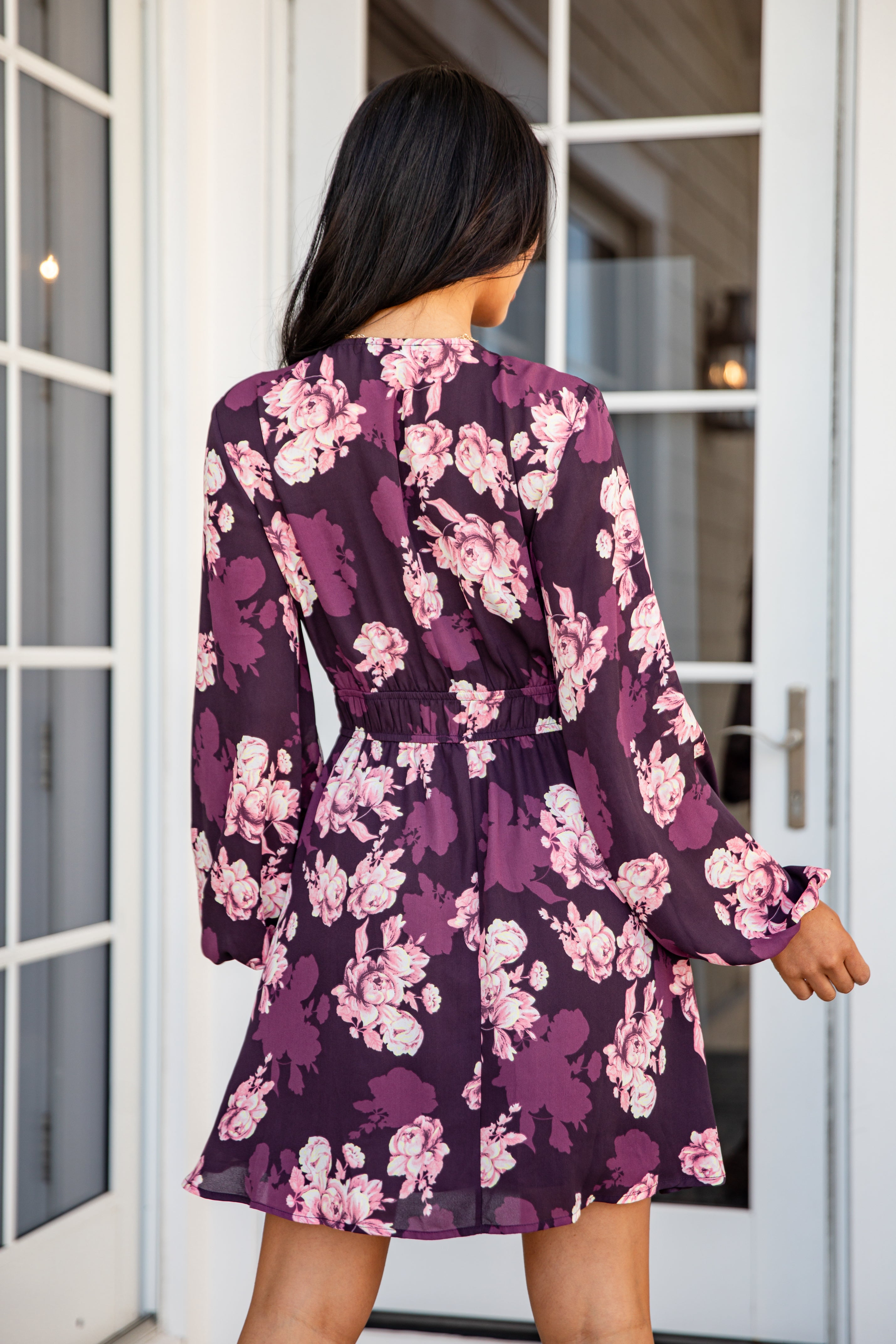 Woman wearing a purple floral dress standing in front of glass doors.