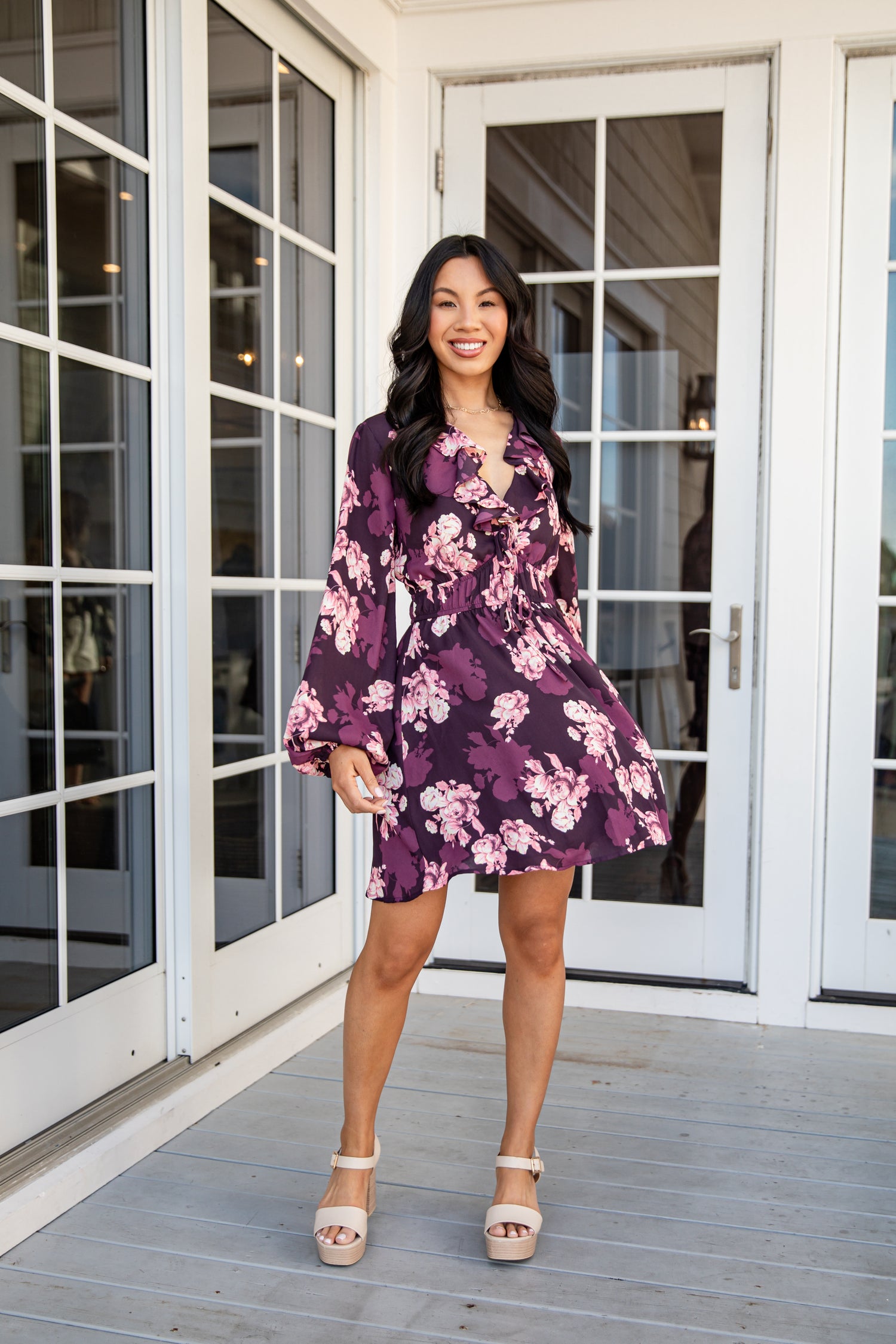 Woman in a purple floral dress standing on a wooden deck.