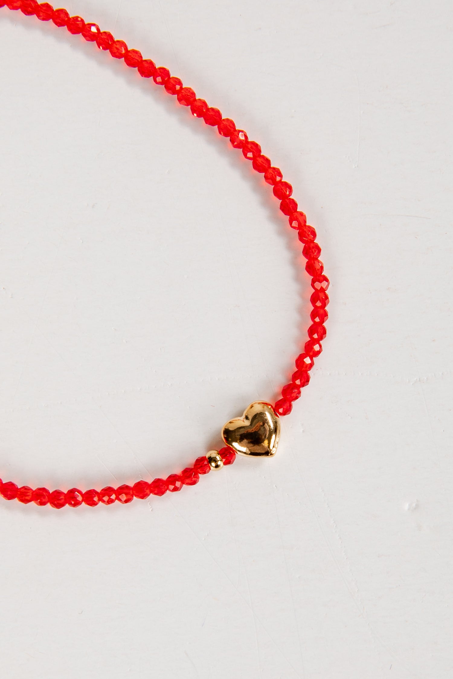 Red beaded necklace with a gold heart charm on a white background