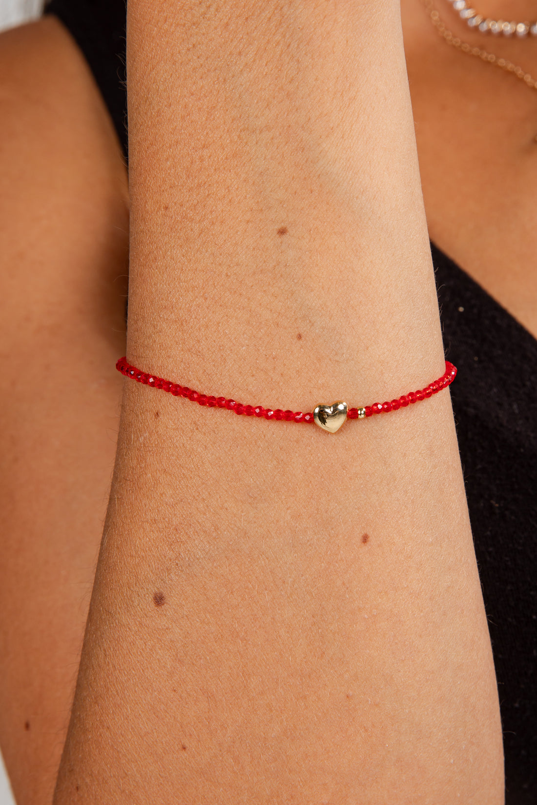 Red beaded bracelet with a gold heart charm on a wrist.
