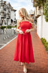 Woman in a red dress standing on a brick sidewalk with buildings in the background