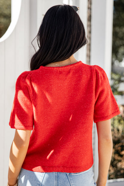 Person wearing a red sweater standing against a white fence.
