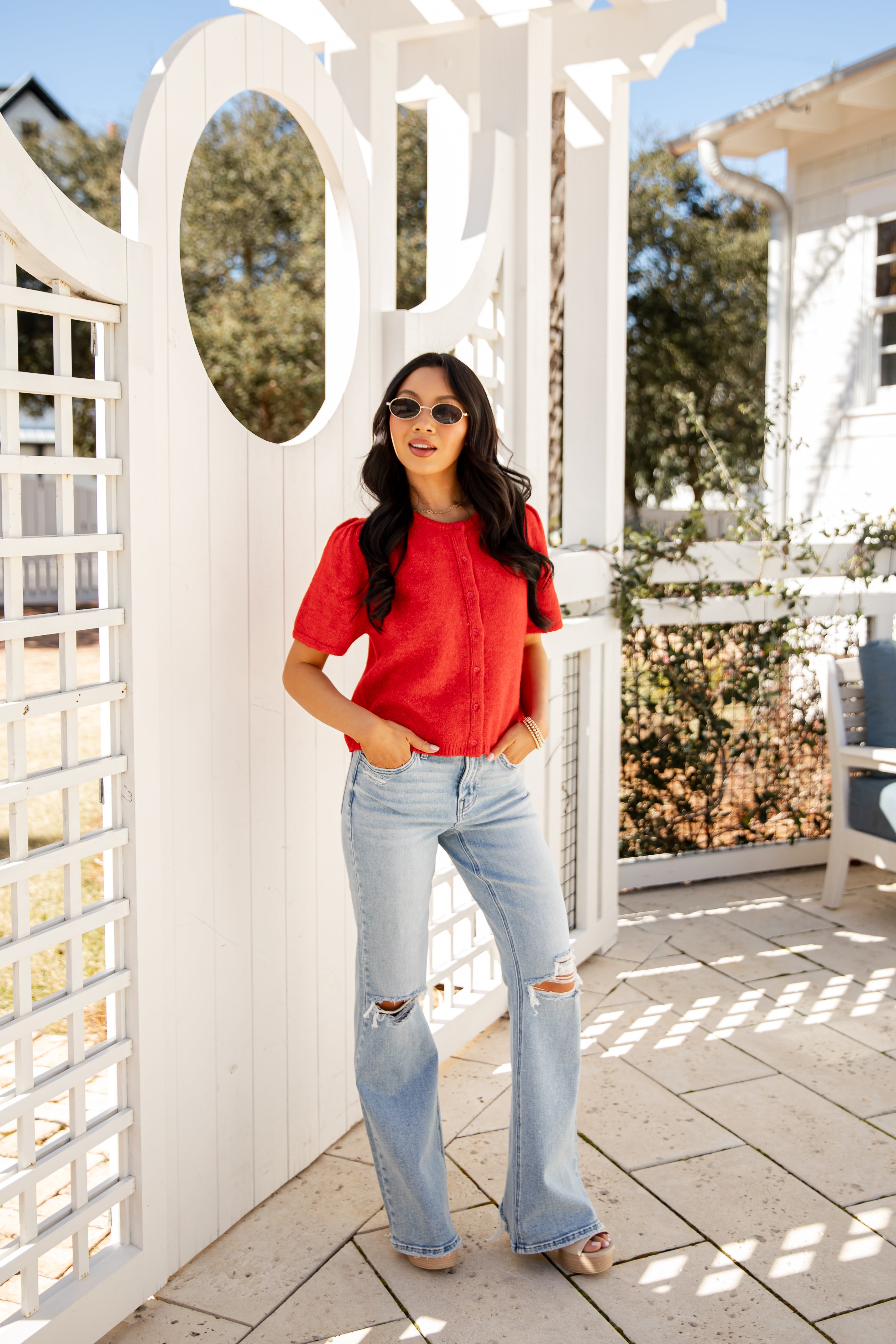 Woman in a red shirt and light blue jeans standing in front of a white lattice structure.