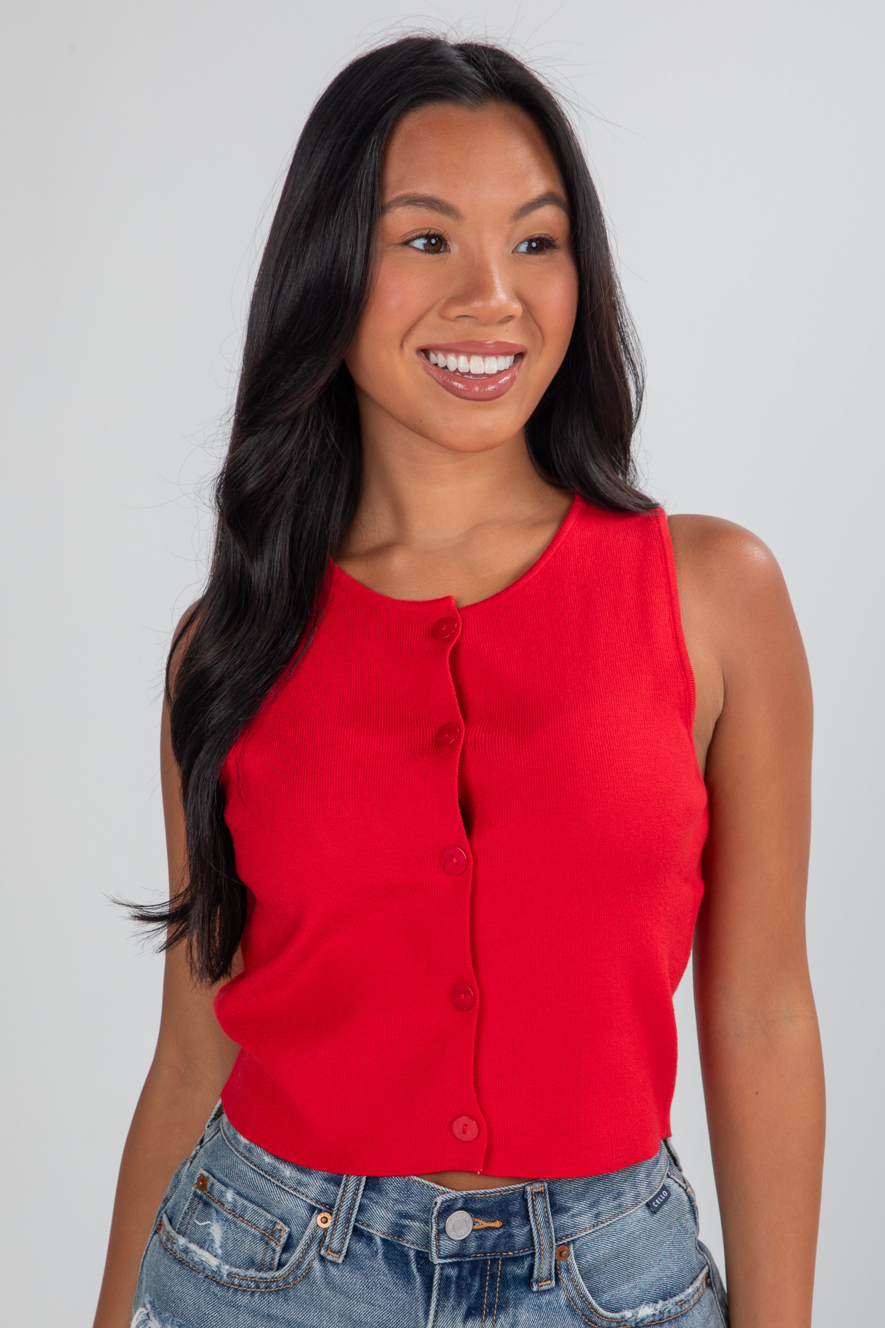 Woman wearing a red sleeveless top and blue jeans against a plain background