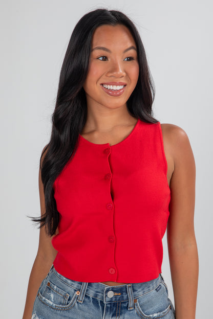 Woman wearing a red sleeveless top and blue jeans against a plain background