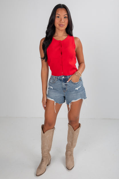 Woman wearing a red top, denim shorts, and beige knee-high boots on a white background