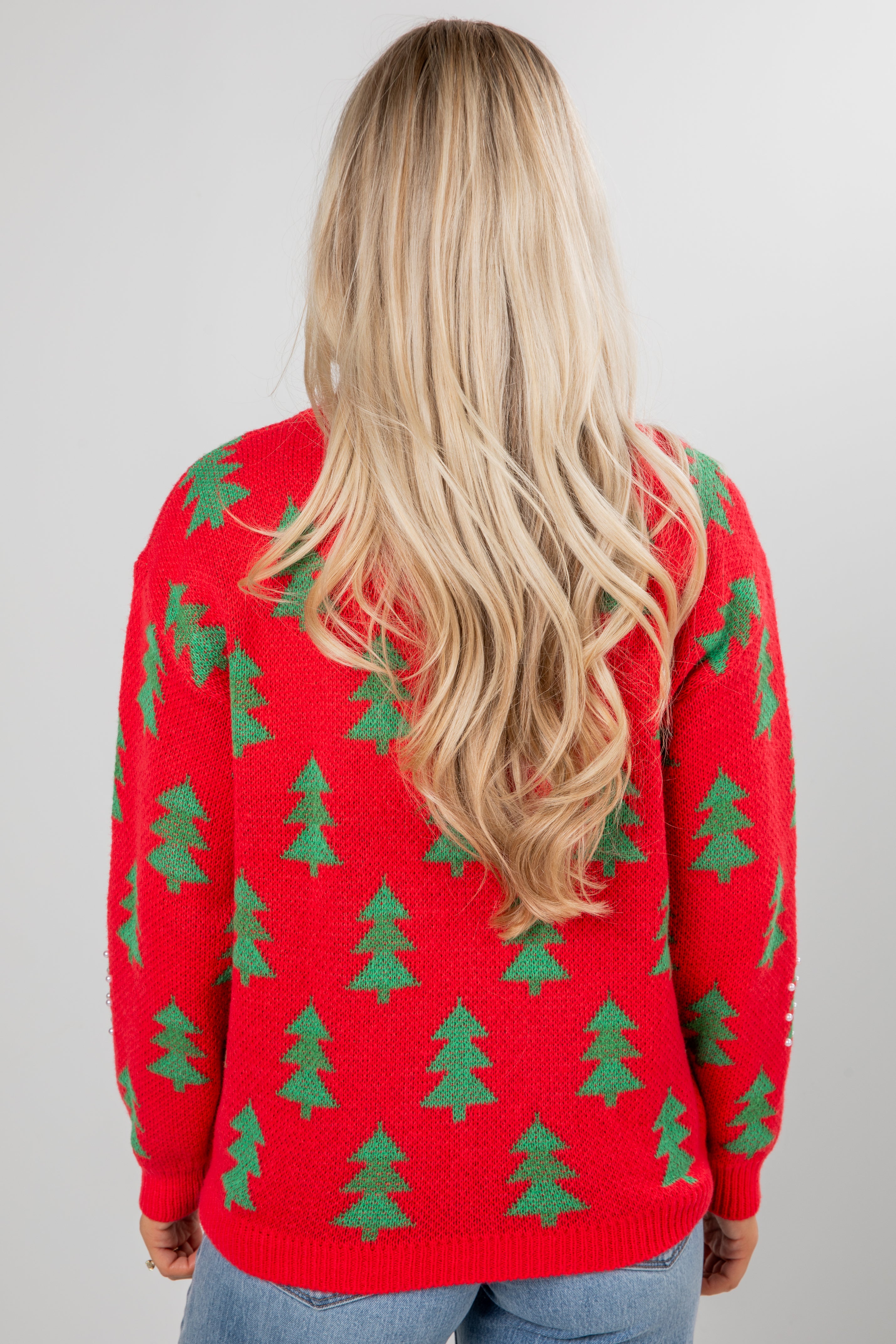 Person wearing a red sweater with green tree patterns on a plain background