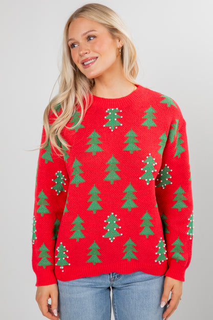 Person wearing a red sweater with green tree patterns on a plain background