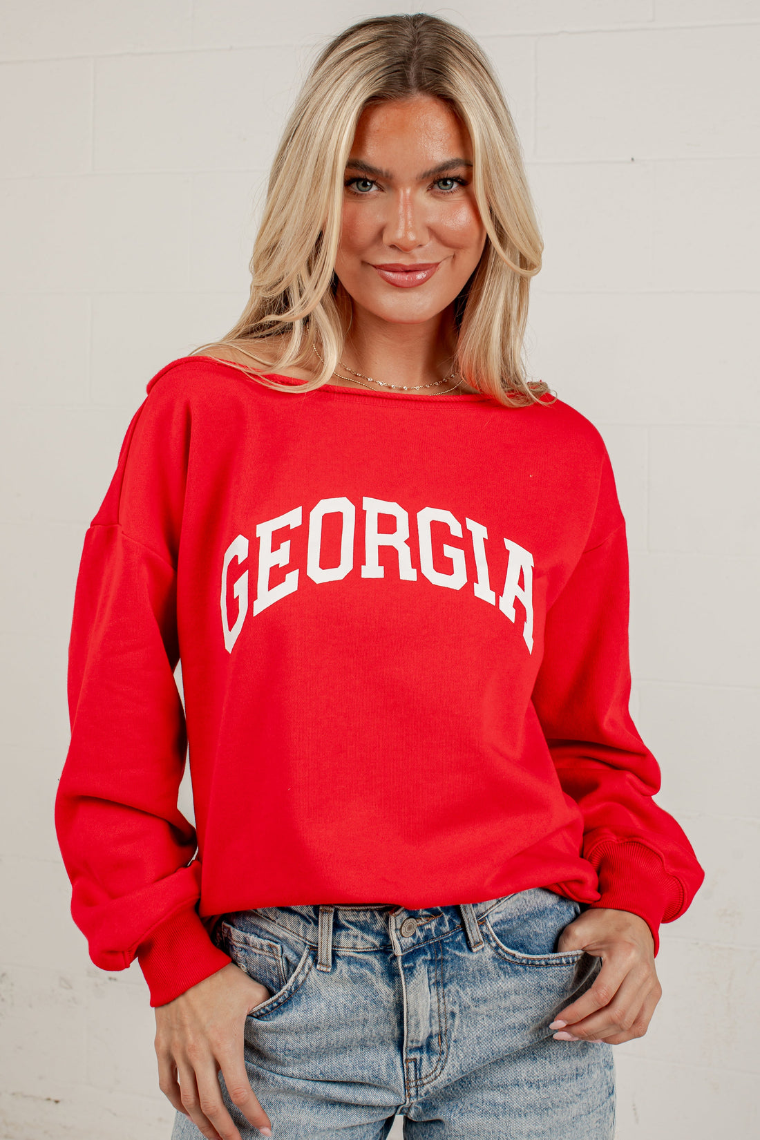 A blonde woman wearing a bright red crewneck sweatshirt with &