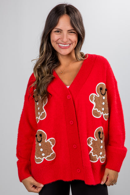 Woman wearing a red cardigan with gingerbread man patterns on a plain background