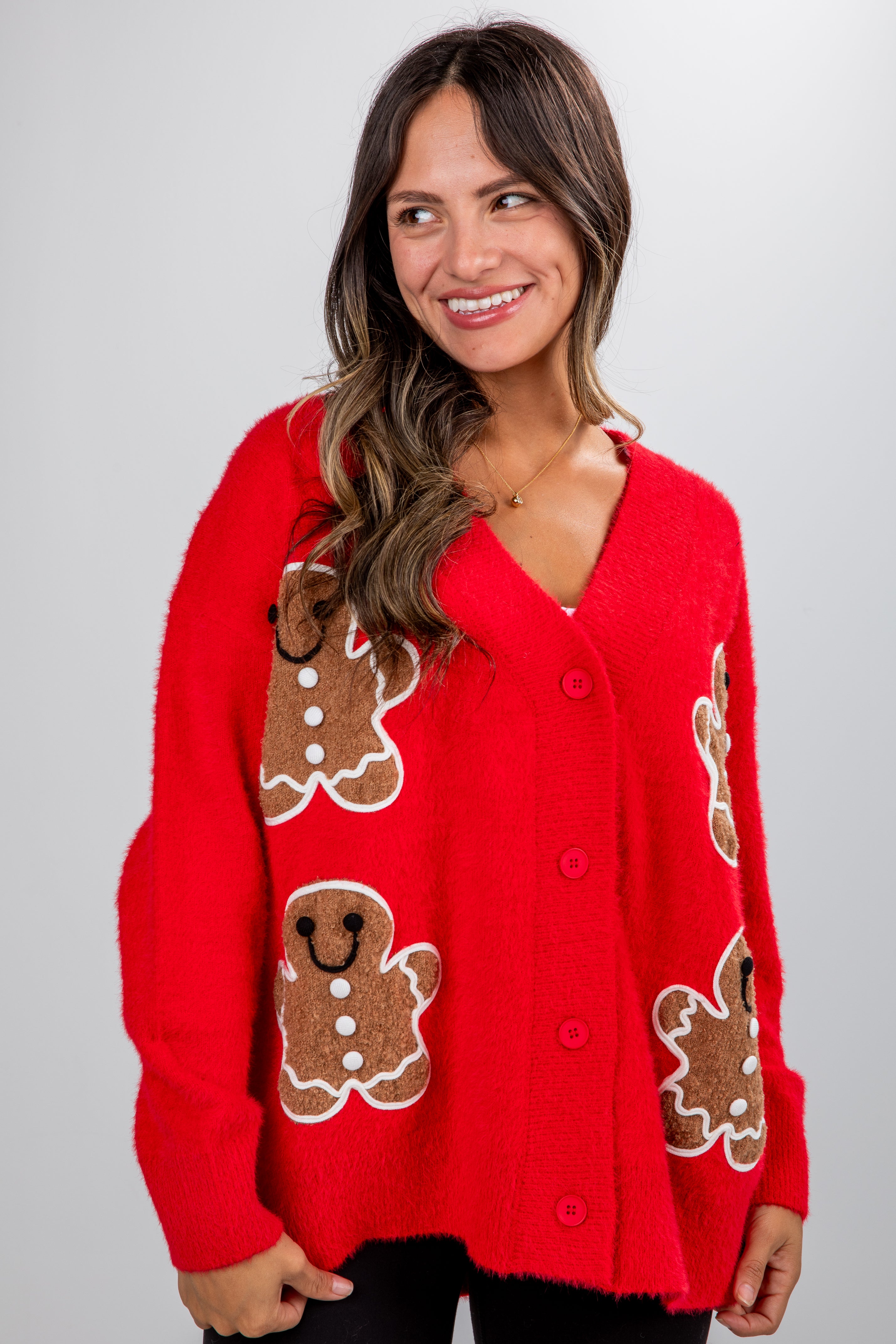 Woman wearing a red sweater with gingerbread man designs on a plain background