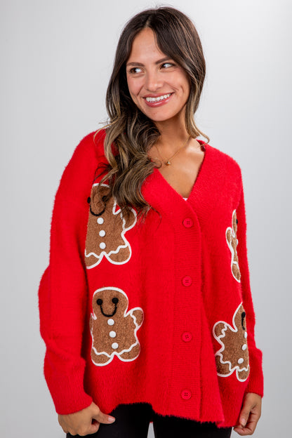 Woman wearing a red sweater with gingerbread man designs on a plain background