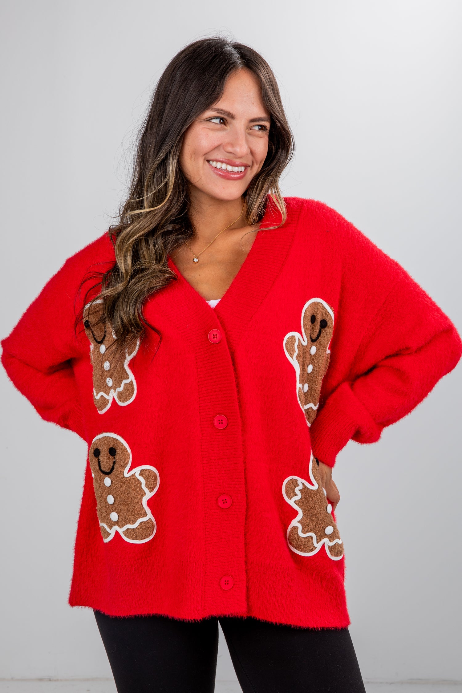 Woman wearing a red sweater with gingerbread man designs on a plain background