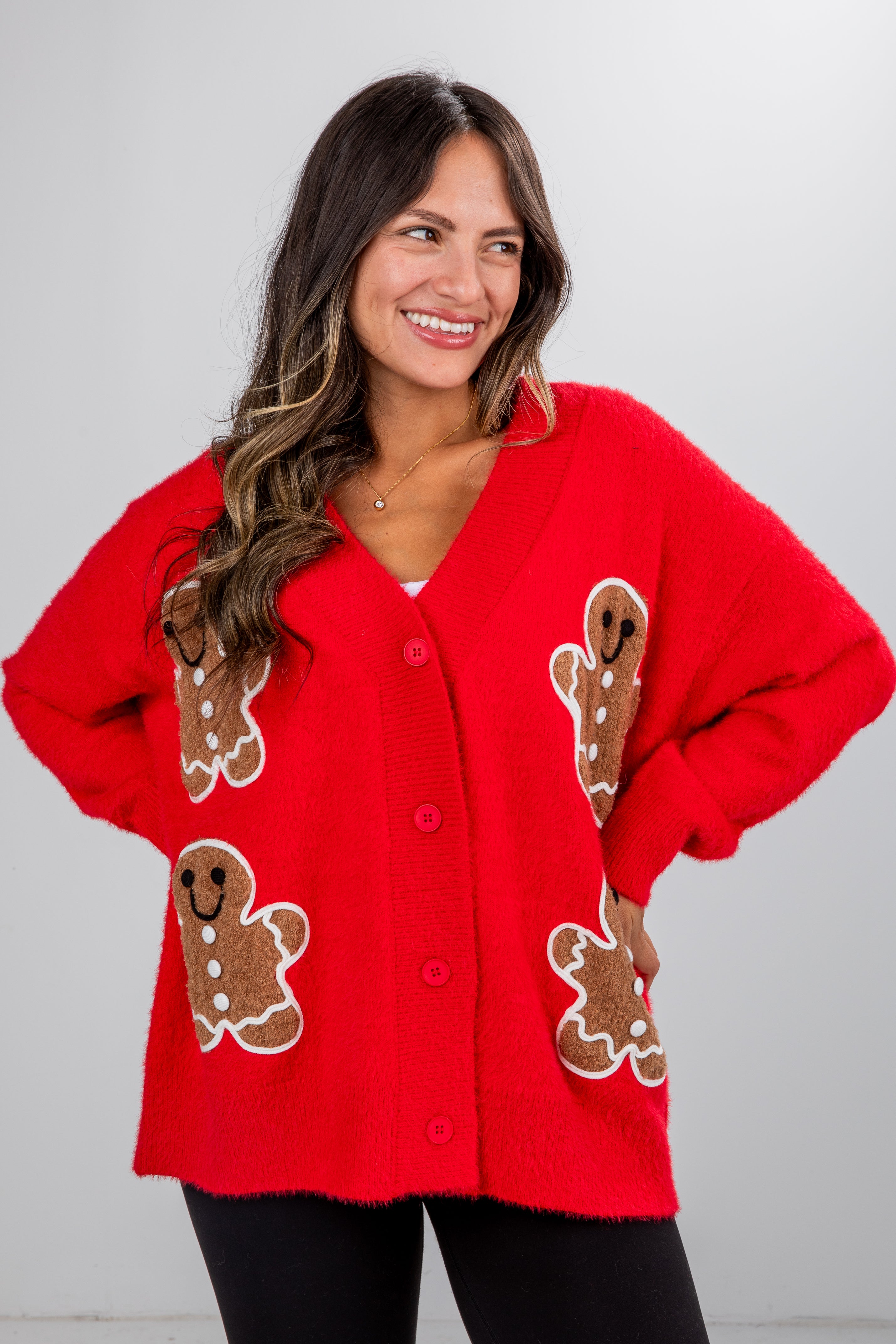 Woman wearing a red sweater with gingerbread man designs on a plain background