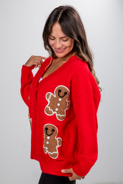 Woman wearing a red sweater with gingerbread man designs on a plain background