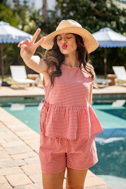 Woman in a red checkered outfit and sun hat by a pool