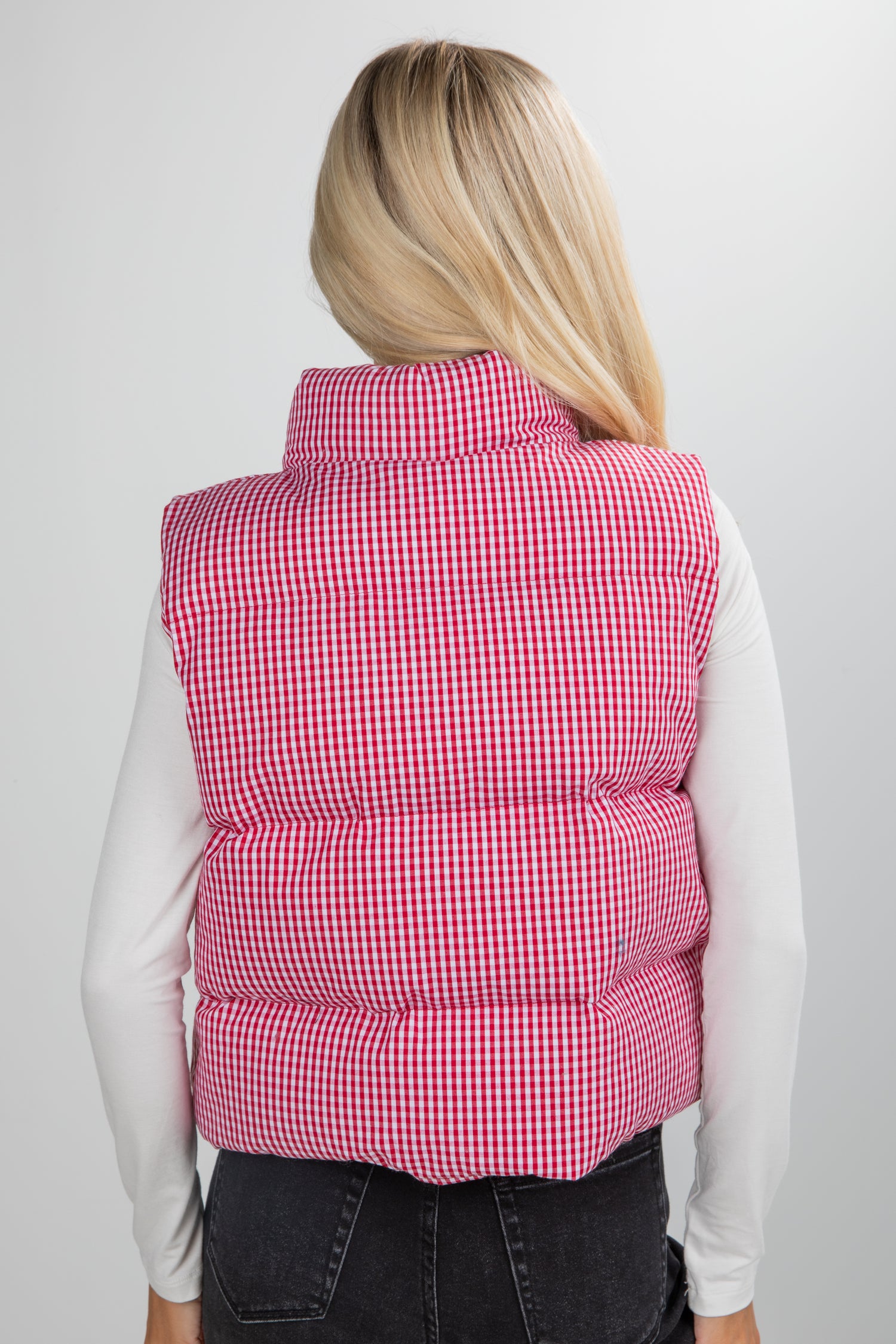Person wearing a red checkered puffer vest on a plain background