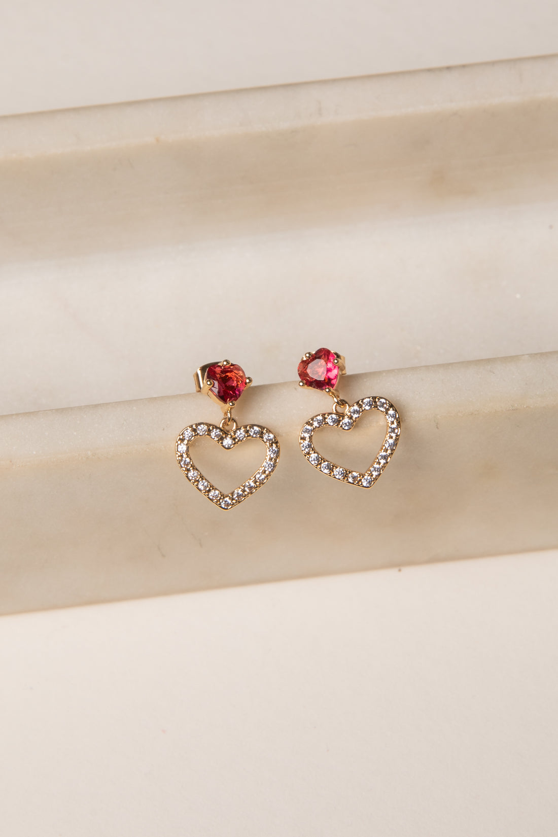 Heart-shaped earrings with red gemstones on a beige fabric background