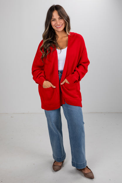 Woman wearing a red cardigan over a white shirt and blue jeans on a white background