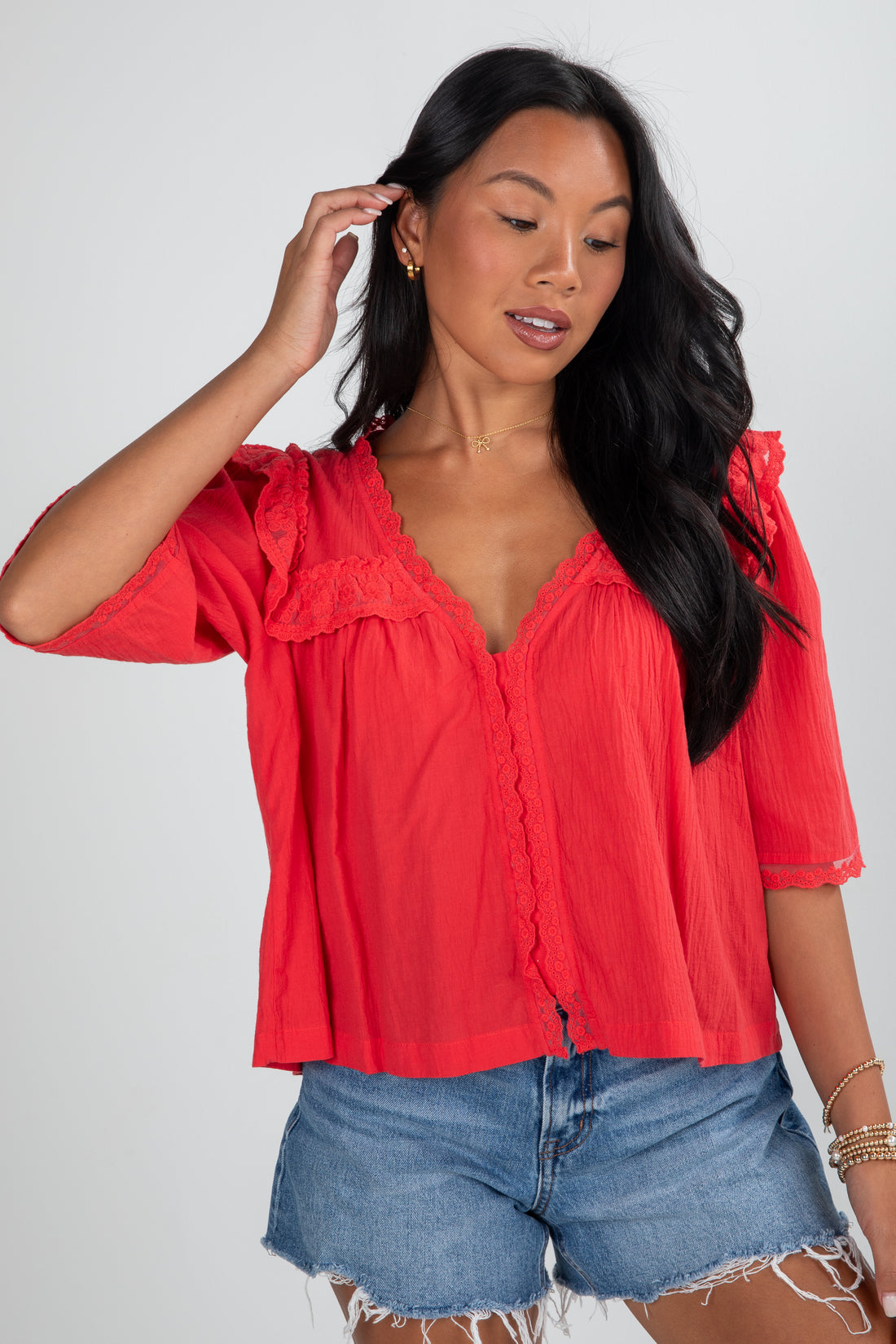 Woman wearing a red blouse and denim shorts against a plain background