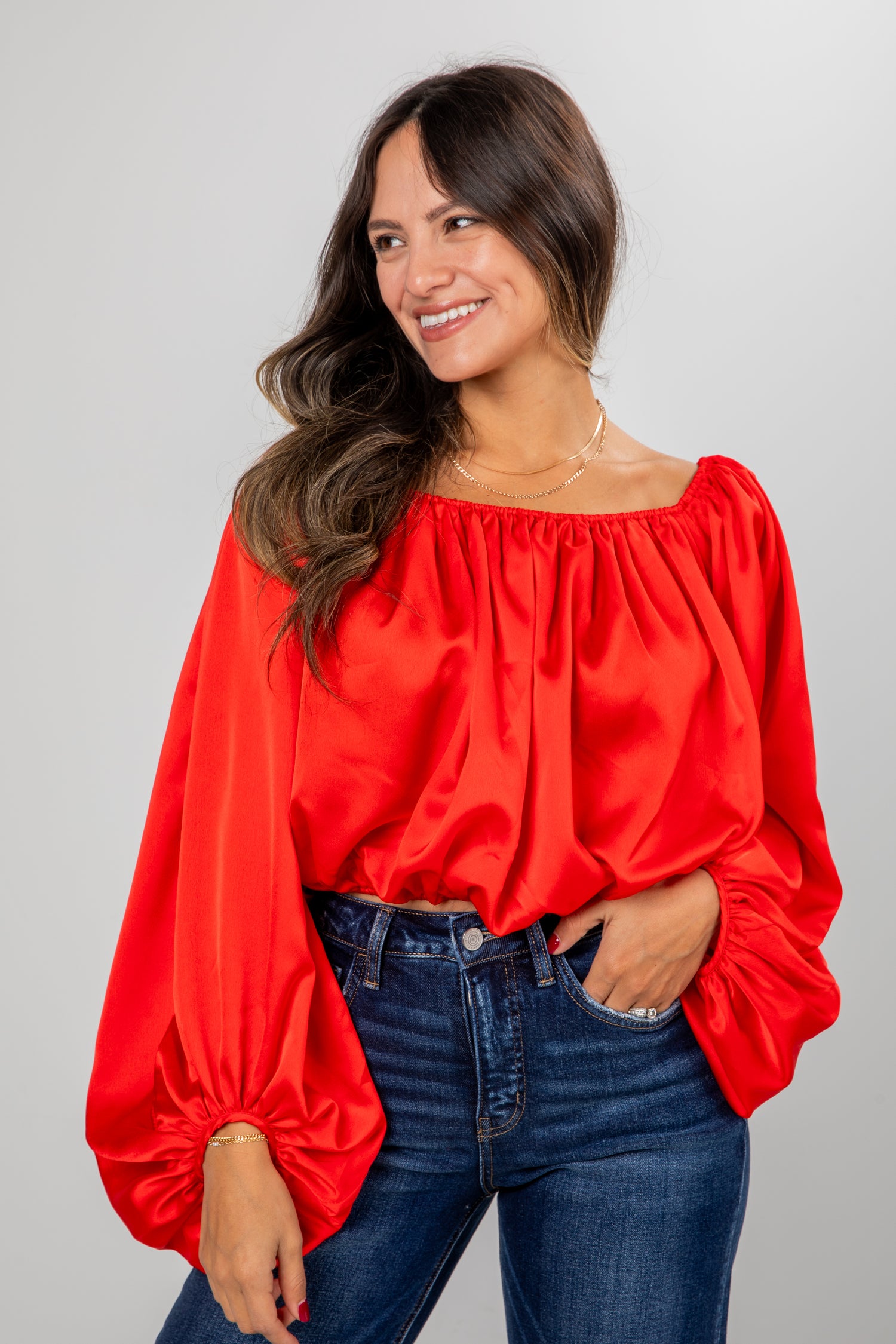Woman wearing a red blouse and blue jeans against a gray background