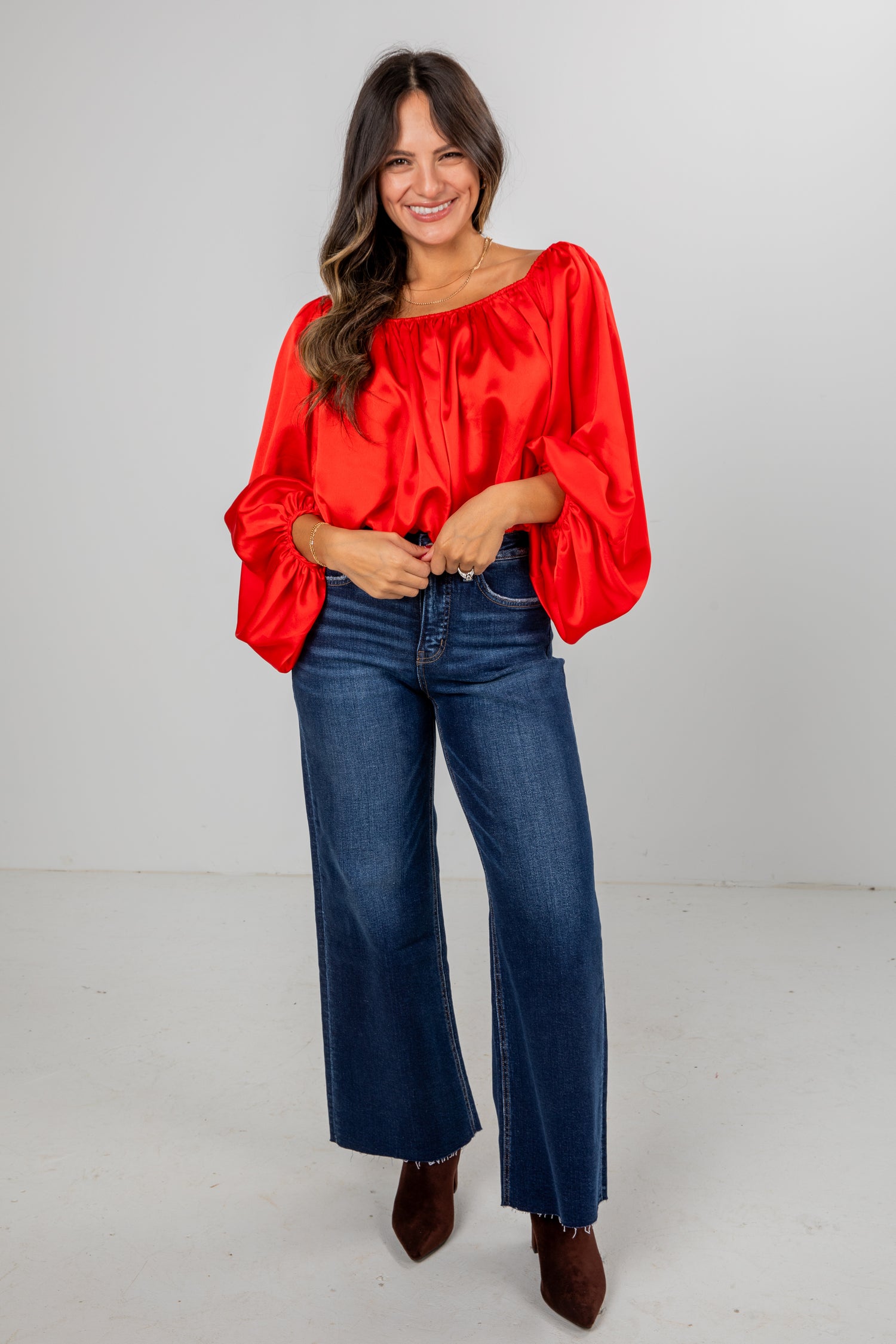 Woman wearing a red blouse and blue jeans on a plain background