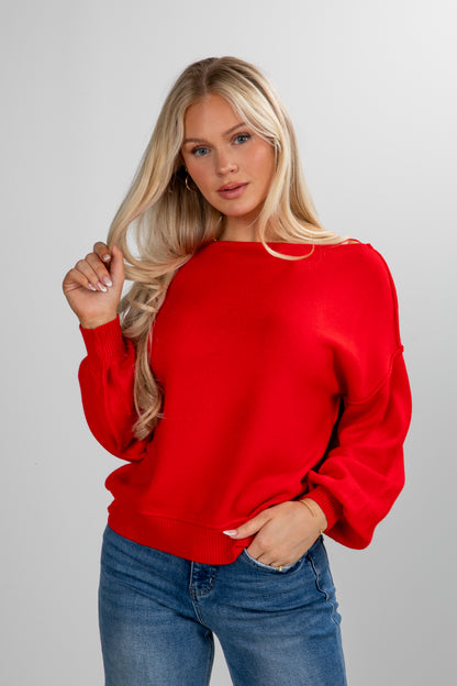 Woman wearing a red sweater and blue jeans against a plain background