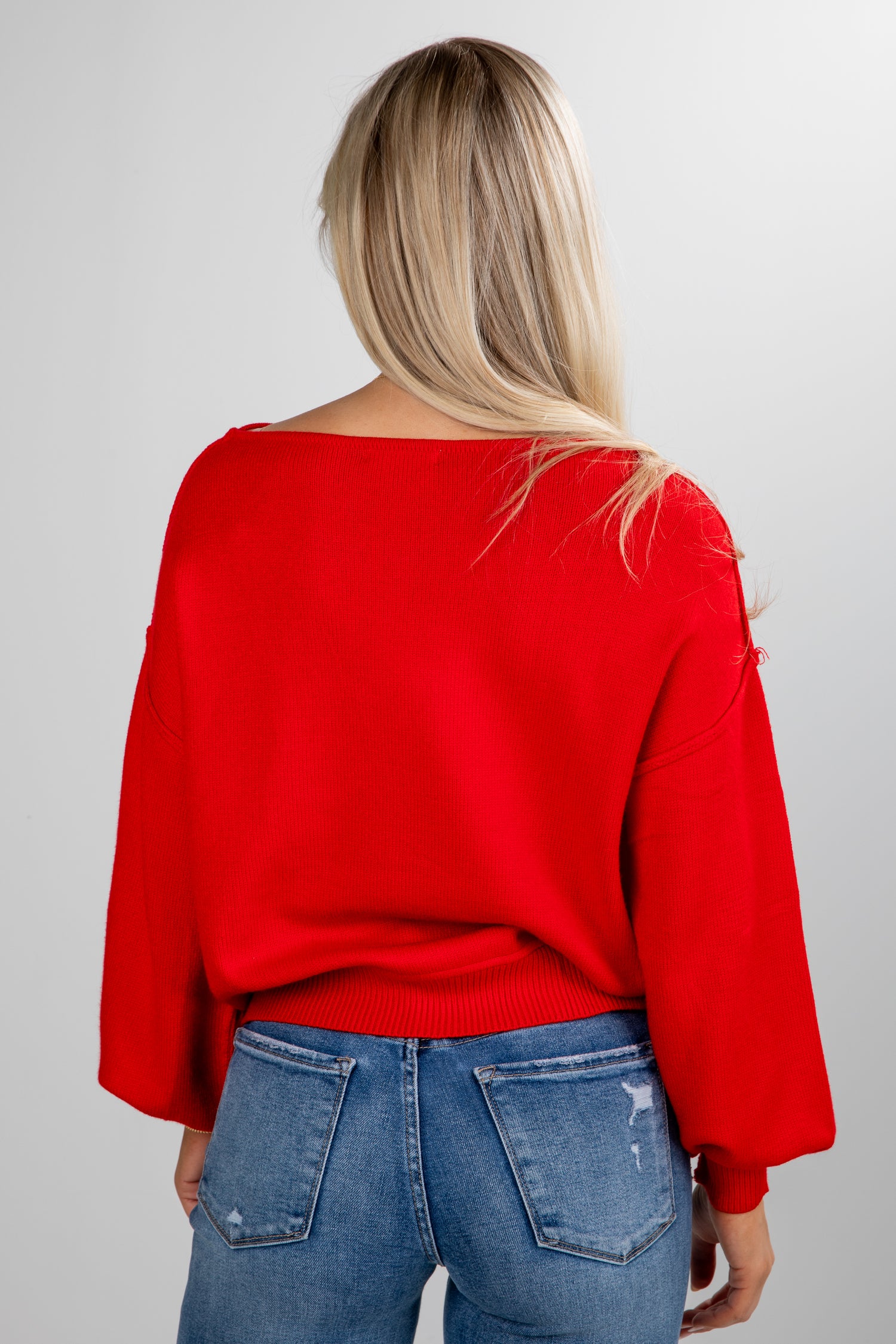 Person wearing a red sweater and blue jeans on a plain background