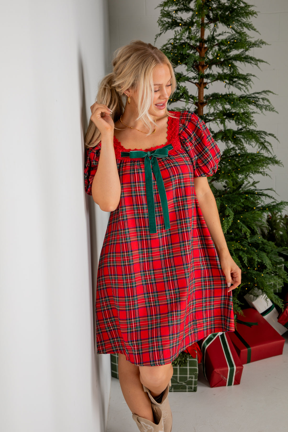Woman in a red plaid dress standing next to a Christmas tree with presents.