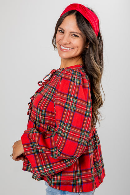 Woman wearing a red plaid shirt and headband against a gray background