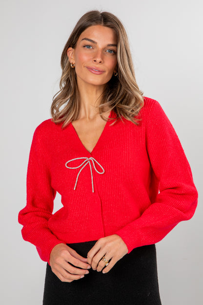 Woman wearing a red sweater with a white bow detail on a gray background