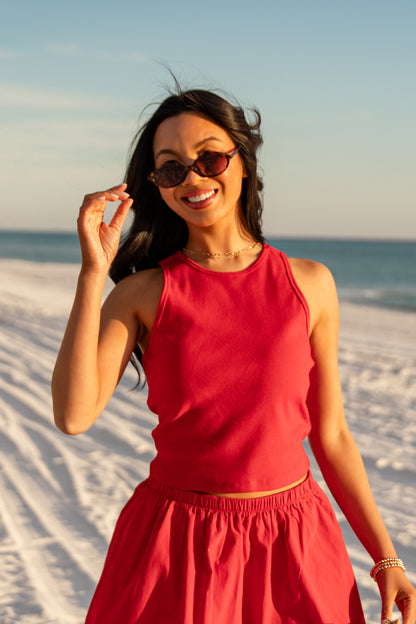Woman in a red dress standing on a sandy beach with ocean view