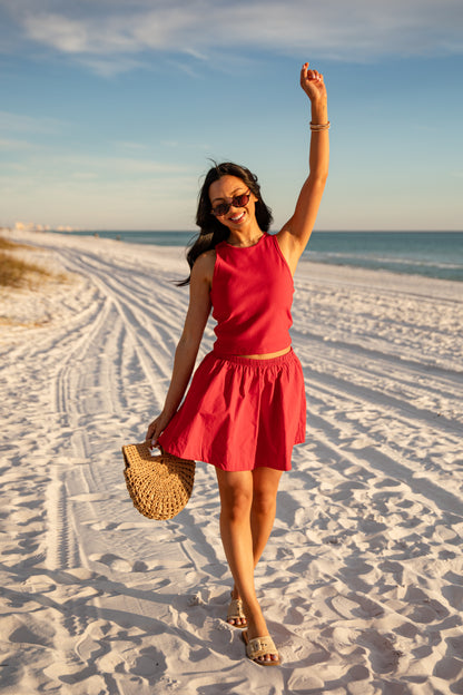Woman in a red dress on a sandy beach with a straw bag