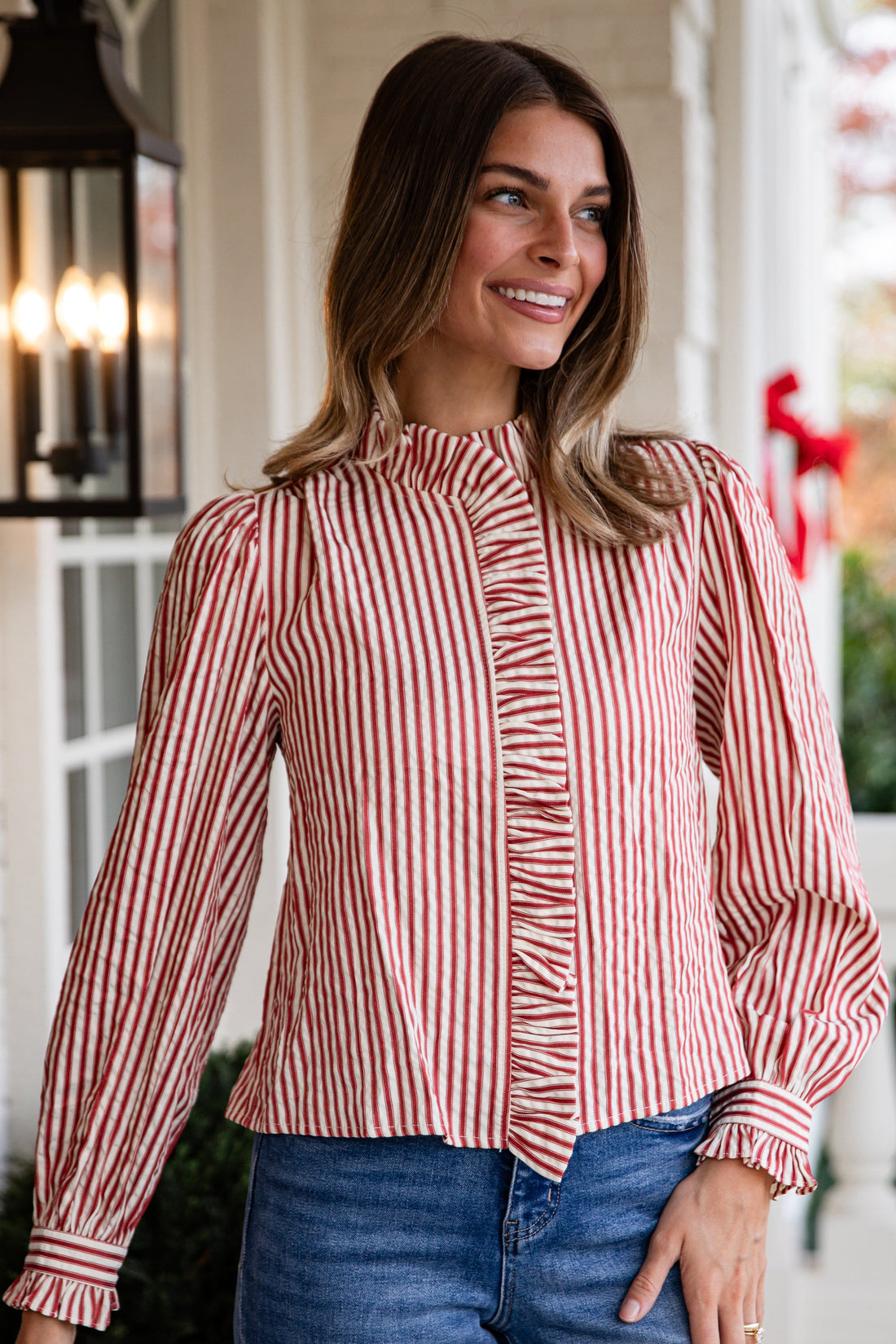 Woman wearing a red and white striped blouse and blue jeans standing on a porch.