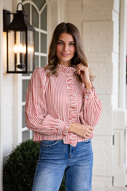 Woman wearing a red and white striped blouse and blue jeans standing outdoors.