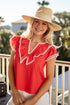 Woman wearing a red top with white trim and a straw hat on a balcony.