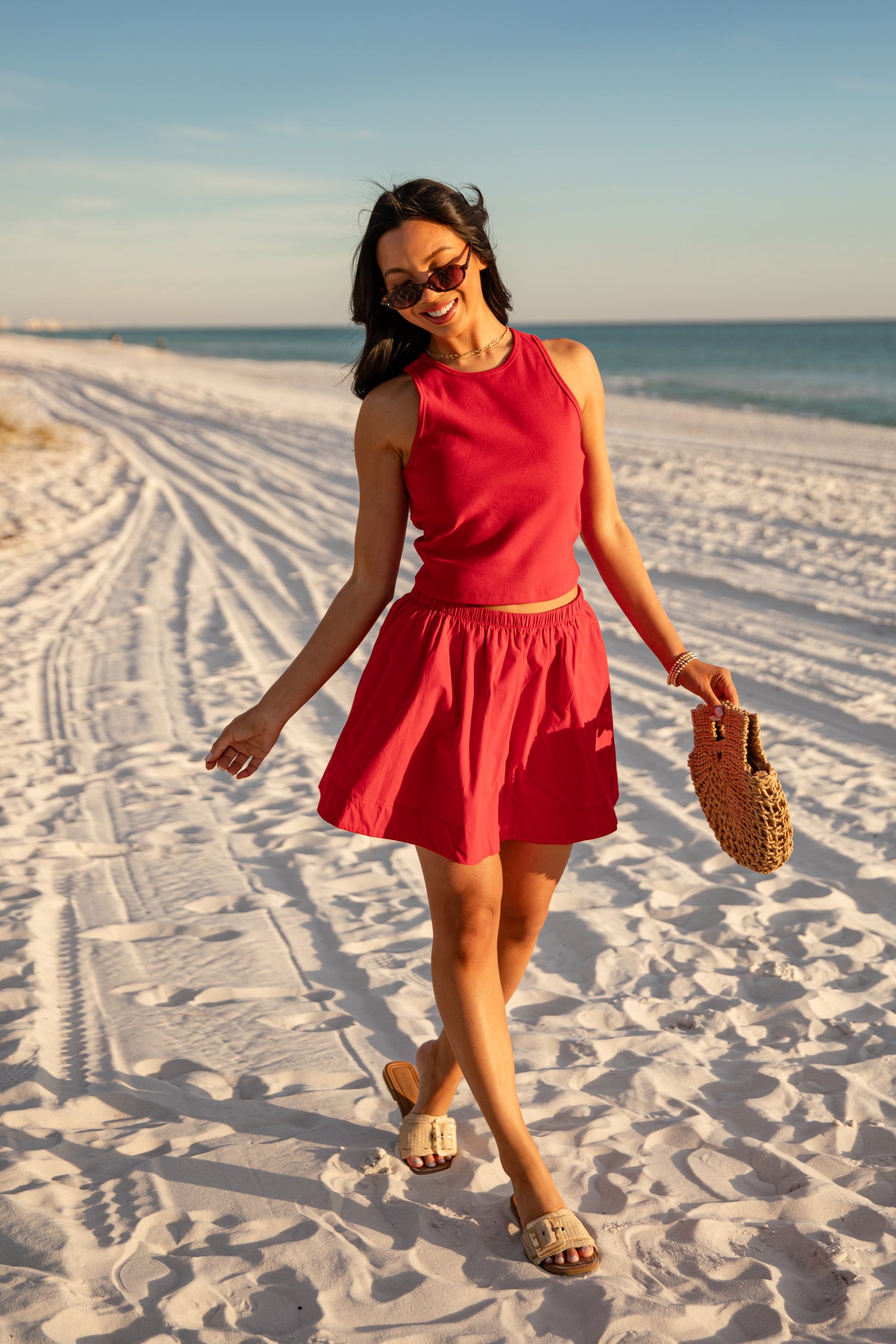 Woman in a red dress walking on a sandy beach with ocean in the background