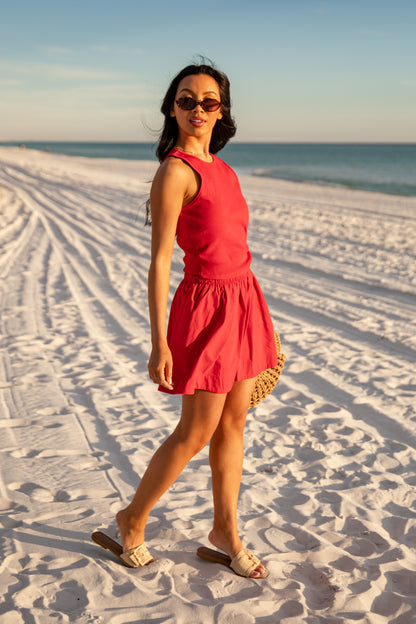 Woman in a red skirt standing on a sandy beach with ocean in the background