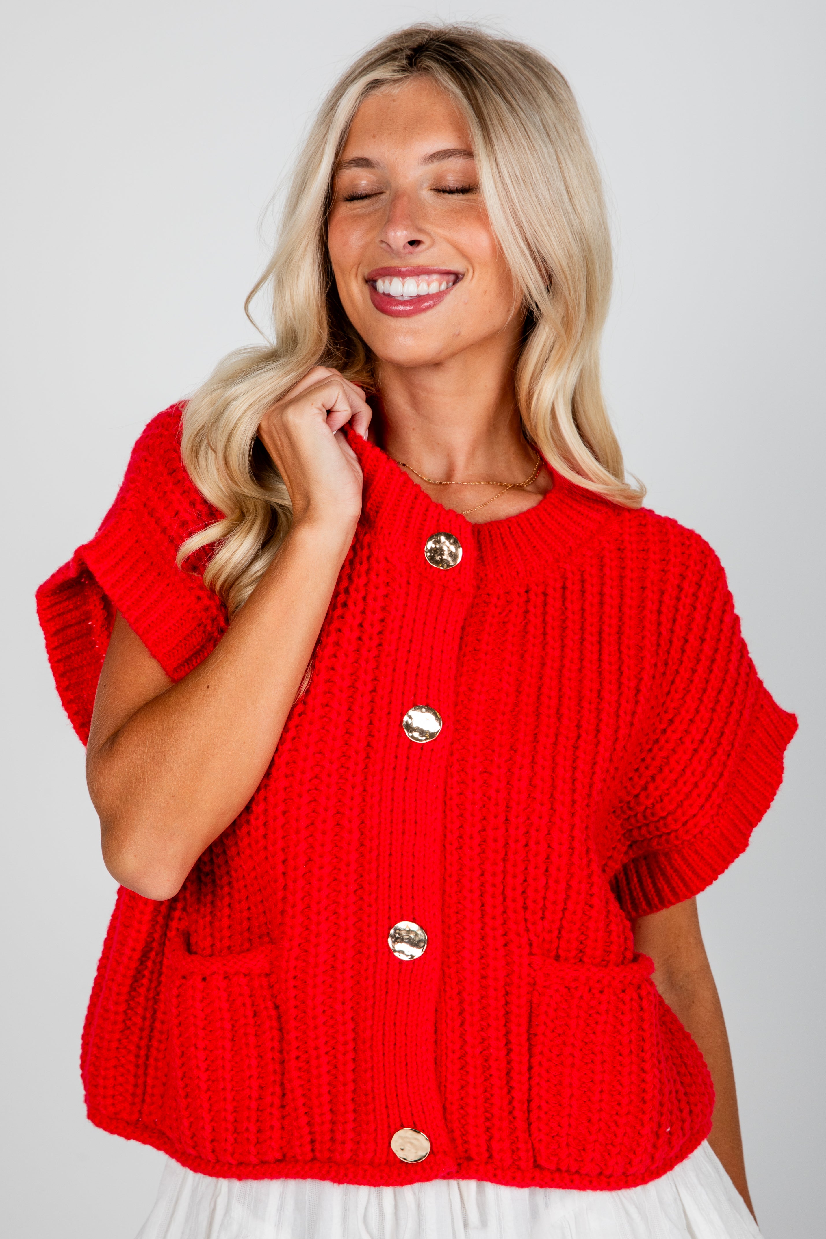 Woman wearing a red knitted cardigan with gold buttons on a white background