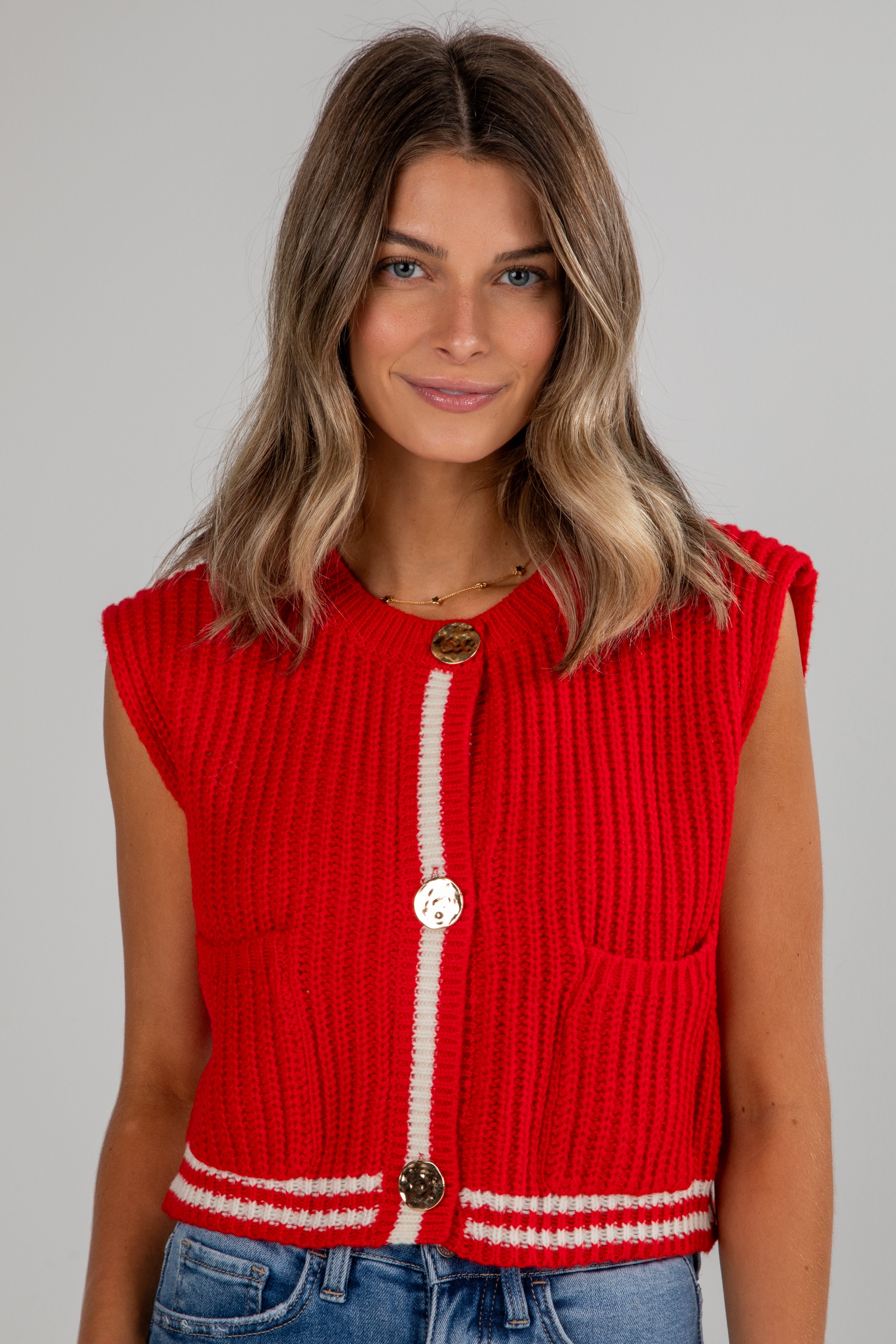 Woman wearing a red knitted vest with white trim on a gray background